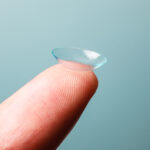 A Contact lens is resting on a finger against a blue background